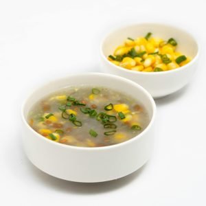 A delectable sweet corn soup garnished with green onions beside a corn salad in white bowls.